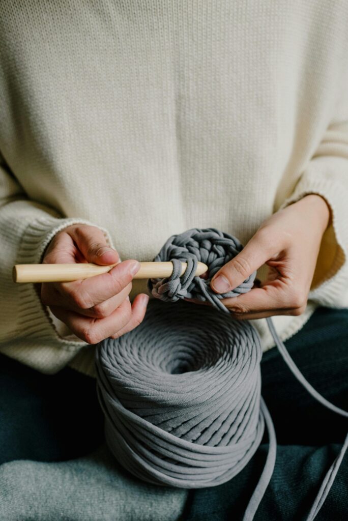 crocheting with grey yarn and a light wood crochet hook